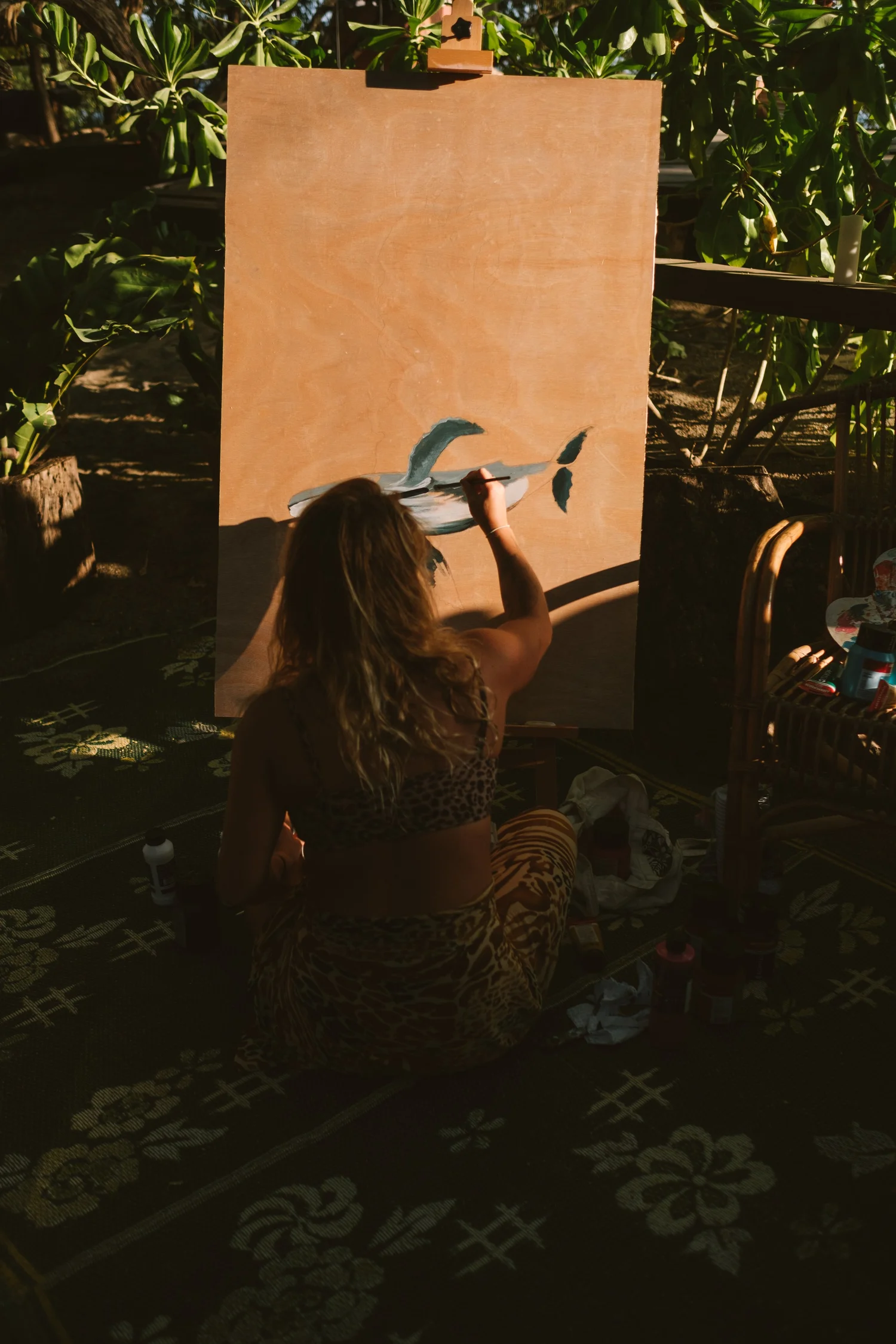 Woman painting a canvas in a garden at sunset