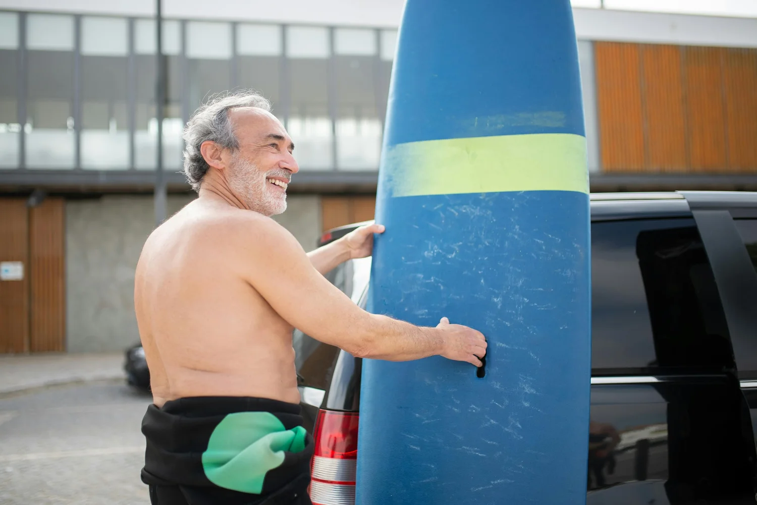 Man holding a blue surfboard beside a car