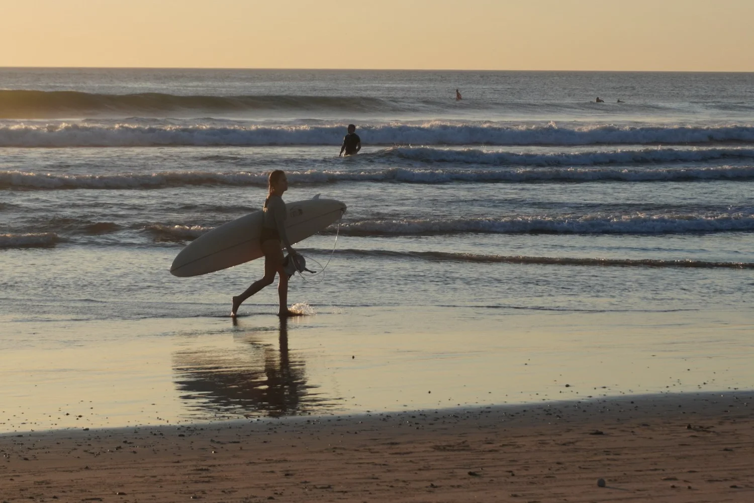 Surfer walking toward the ocean at sunset