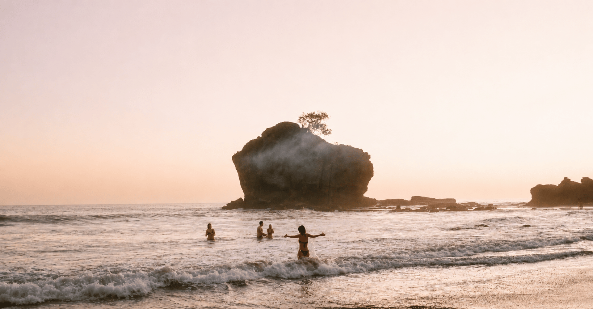 Group of people standing together on a beach at sunset, looking out at the ocean